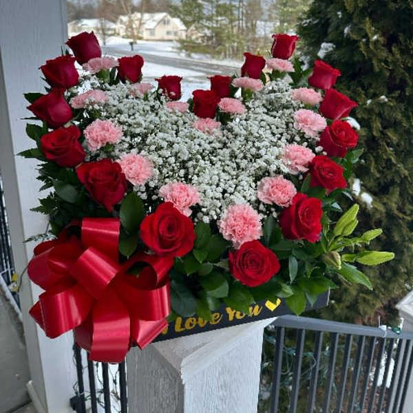 Heart-shaped bouquet of red roses and pink carnations with a red ribbon
