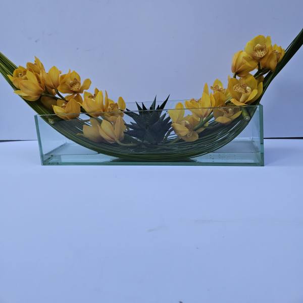 Yellow orchids arranged in a curved glass vase