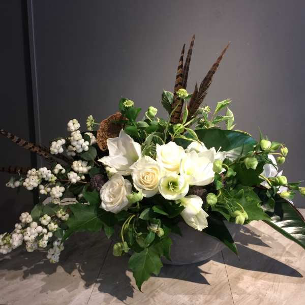 White floral arrangement with berries and feathers in a low container