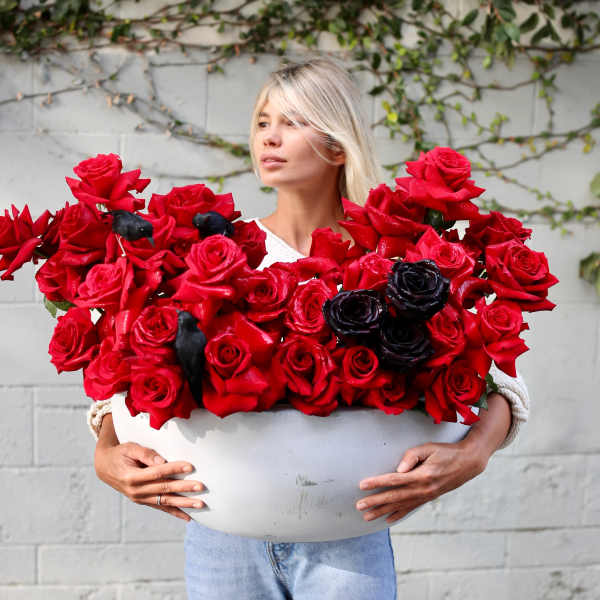 Woman holding a large white bowl of red roses with a few black roses