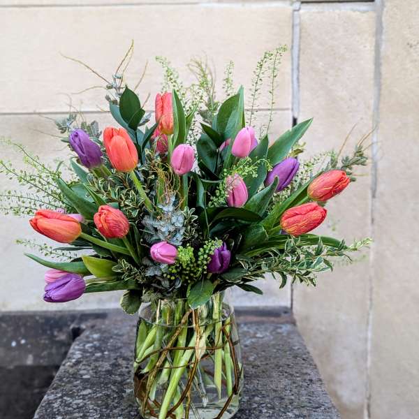 Mixed tulips in pink, purple, and orange arranged in a glass vase