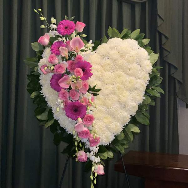 Heart-shaped floral wreath with pink flowers and white blooms on an easel