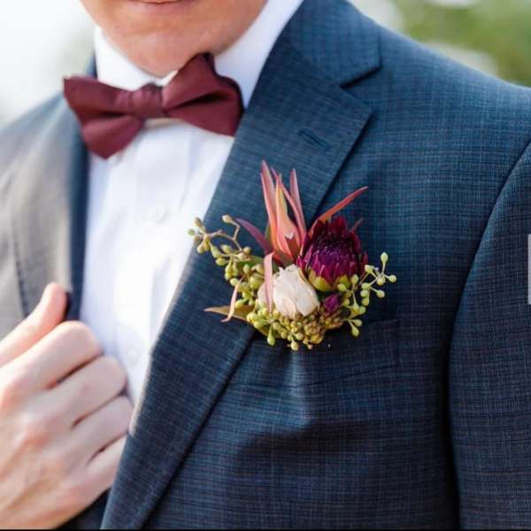 Boutonniere with burgundy and blush flowers on a suit jacket