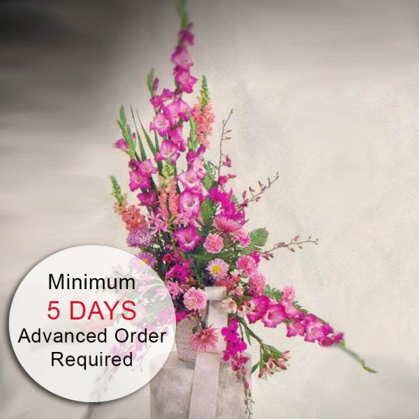Tall pink floral arrangement with gladiolus and mixed flowers in a fabric-wrapped container
