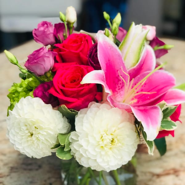 Bouquet of pink lilies, red roses, and white blooms in a glass vase