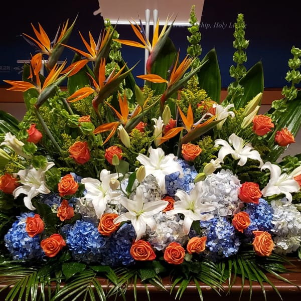 Large altar-style arrangement with orange, blue, and white flowers including lilies and hydrangeas