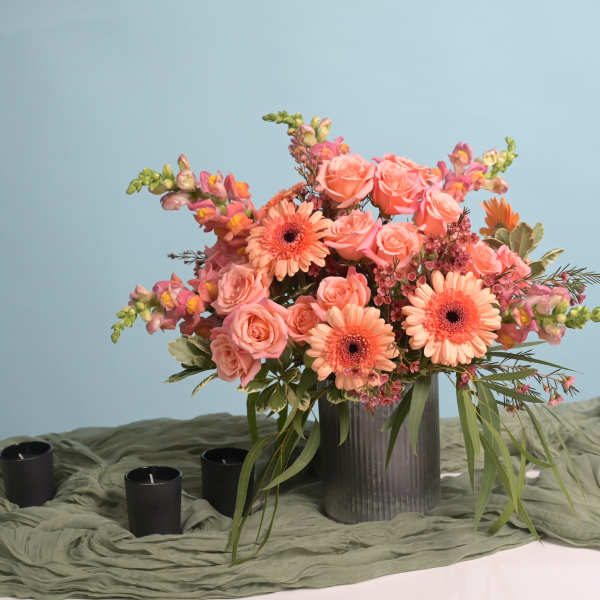 Peach and pink floral arrangement in a ribbed vase with candles nearby