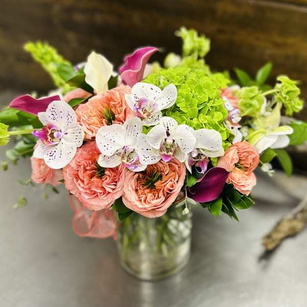 Bouquet of coral roses, white orchids, and green hydrangeas in a glass vase