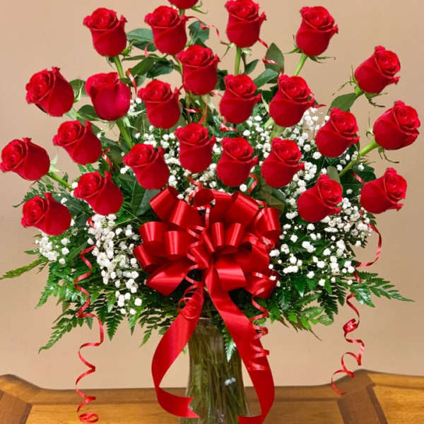Red roses arranged in a clear glass vase with a large red bow
