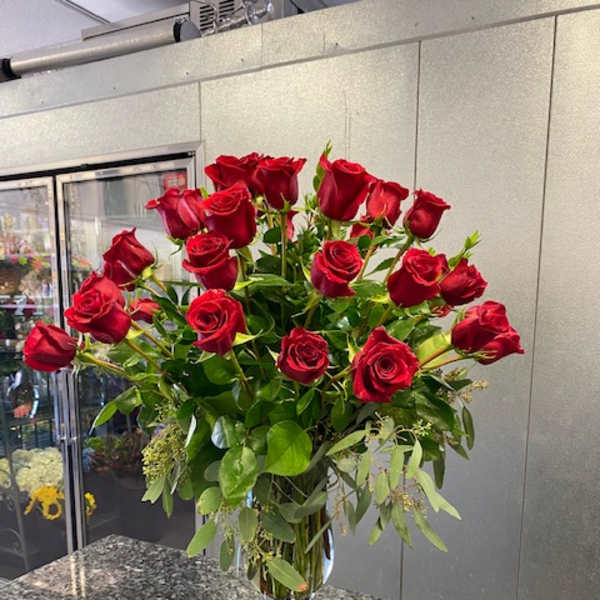 Tall vase arrangement of red roses with greenery
