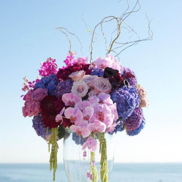 Tall floral arrangement in a clear glass vase with pink, purple, and blue blooms