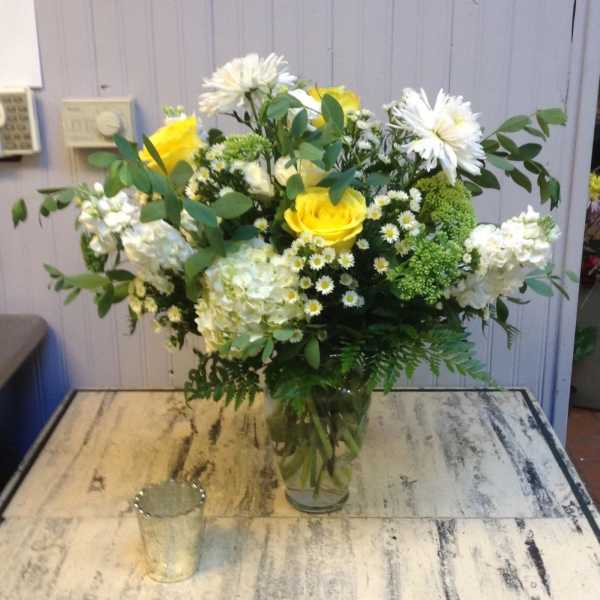 Yellow roses and white flowers arranged in a clear glass vase