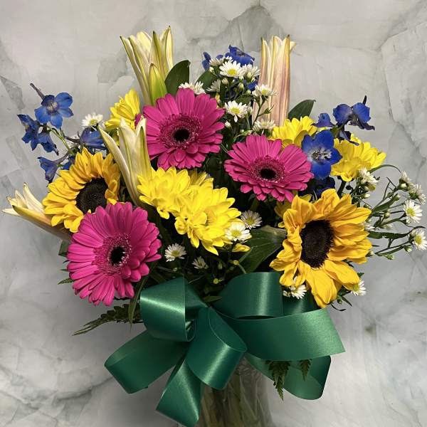Bouquet of sunflowers, pink gerberas, and blue flowers in a glass vase