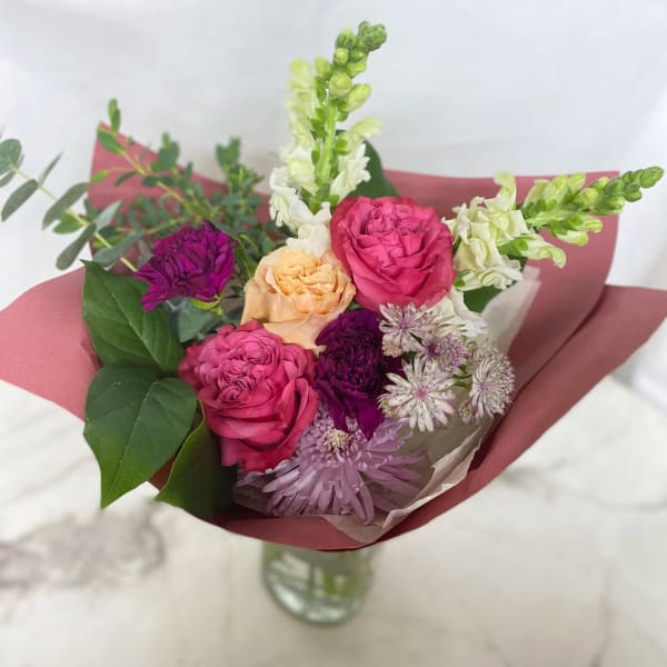 Mixed bouquet of pink, peach, purple, and white flowers in paper wrap
