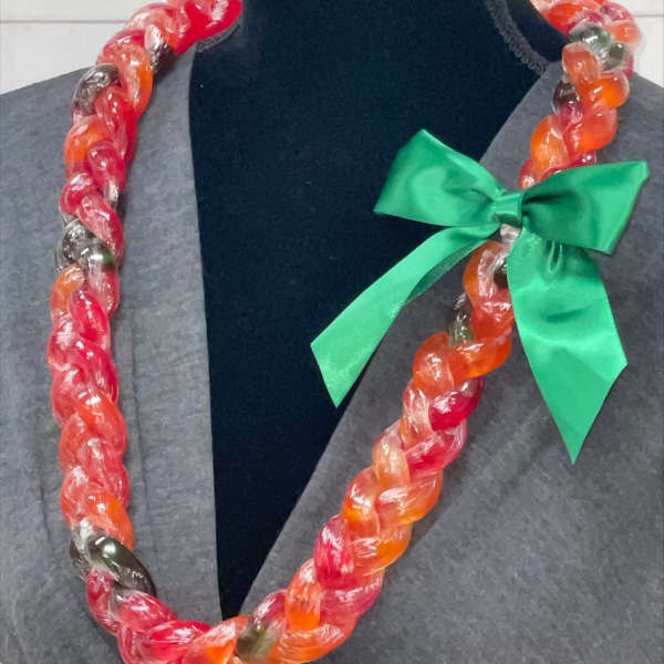 Braided candy lei in red and orange hues with a green satin bow on a display bust.