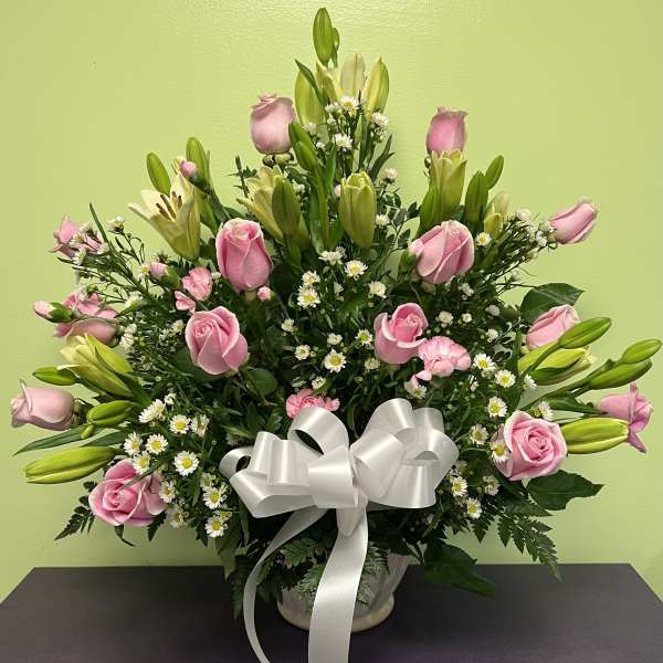 Pink roses and lilies arranged in a vase with a white ribbon bow