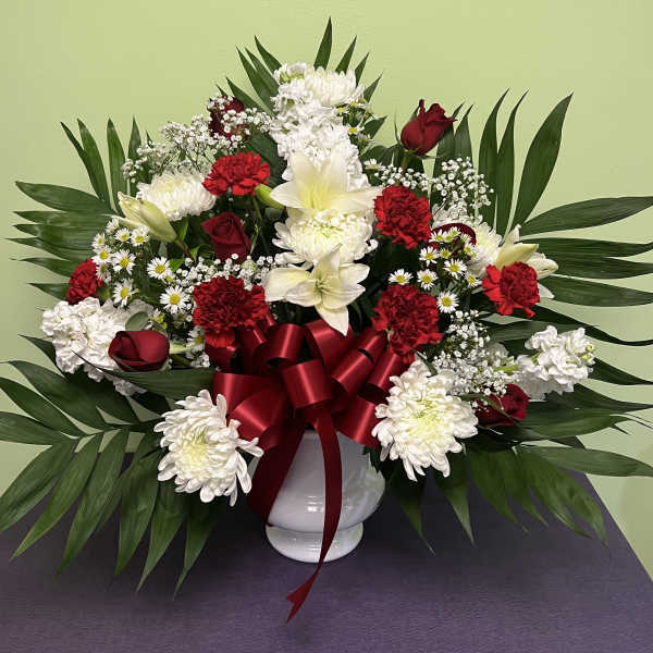Red and white floral arrangement in a white vase with a red ribbon