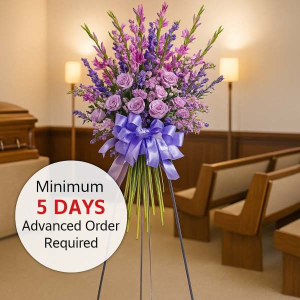 Tall lavender and purple funeral standing spray with roses and ribbon on an easel in a chapel