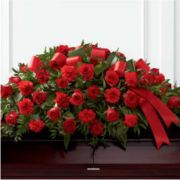 Red roses and carnations arranged on a casket with red ribbon