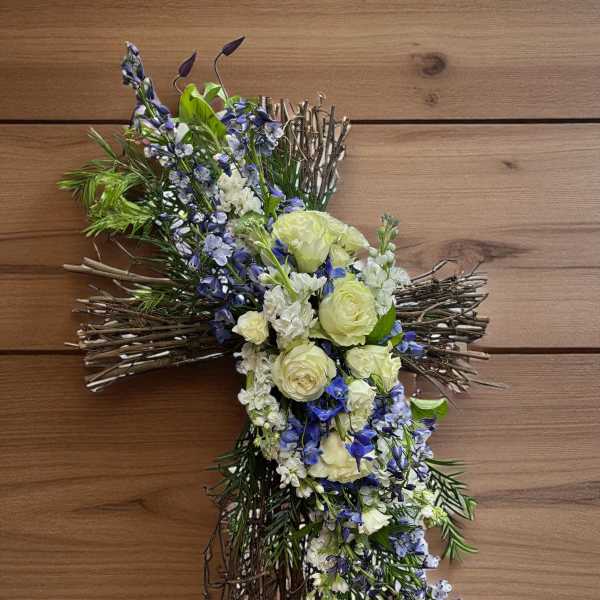 Cross-shaped floral tribute with white and blue flowers on a twig base