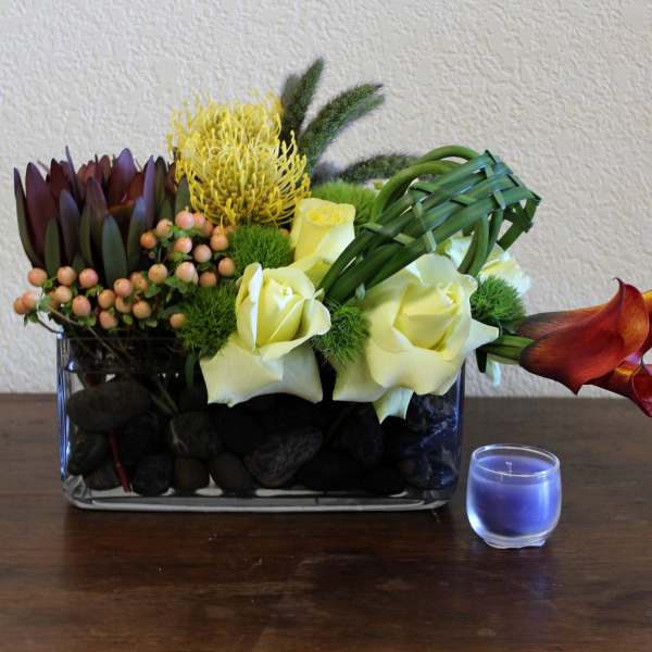 Mixed floral arrangement in a glass vase with a small blue candle beside it