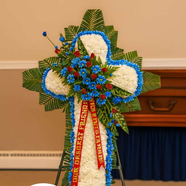 Standing cross-shaped funeral spray of white flowers with blue and red accents on an easel