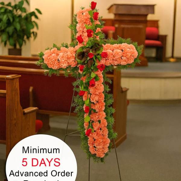 Tall peach carnation cross with red roses and greenery on an easel in a church
