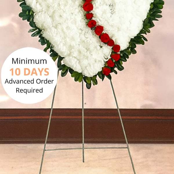 Heart-shaped white funeral wreath with red flowers on a metal stand