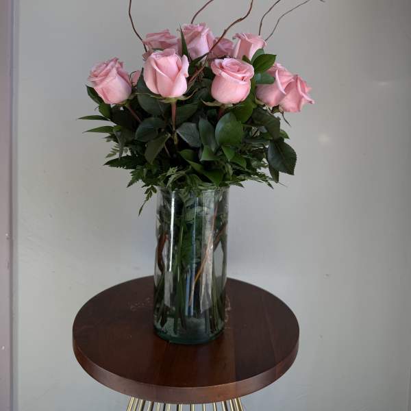 Pink roses arranged in a clear glass vase with tall curly branches