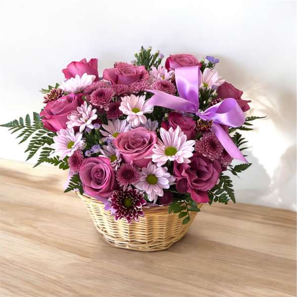 Basket arrangement of mauve roses and pink daisies with a purple ribbon bow