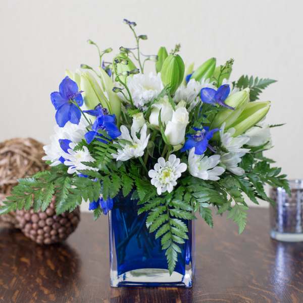 Blue vase with white and blue flowers and green foliage