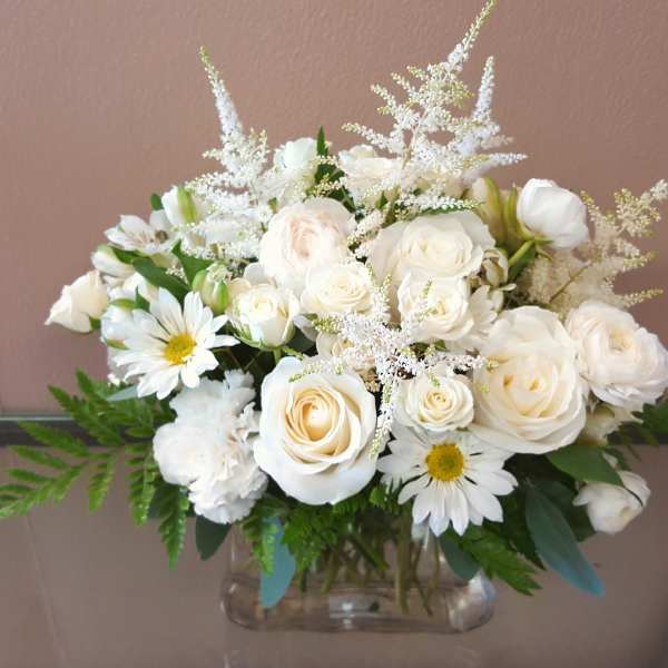 White roses and daisies arranged in a clear glass vase