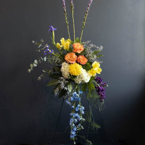 Tall mixed flower arrangement with orange, yellow, blue, and purple blooms