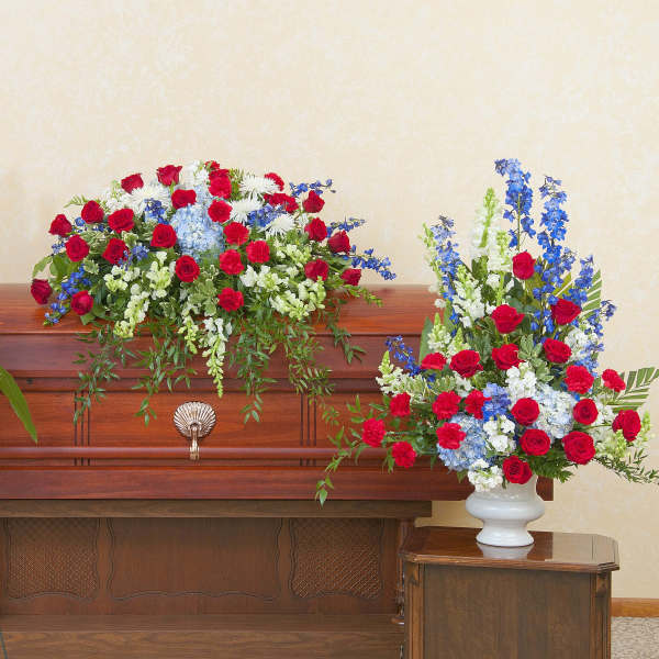 Red, white, and blue funeral floral set with casket spray and side arrangements on a wooden casket