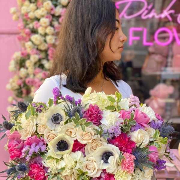Woman holding a large bouquet of pink, cream, and purple flowers in a hatbox