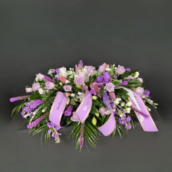 Lavender and white floral casket spray with ribbon accents