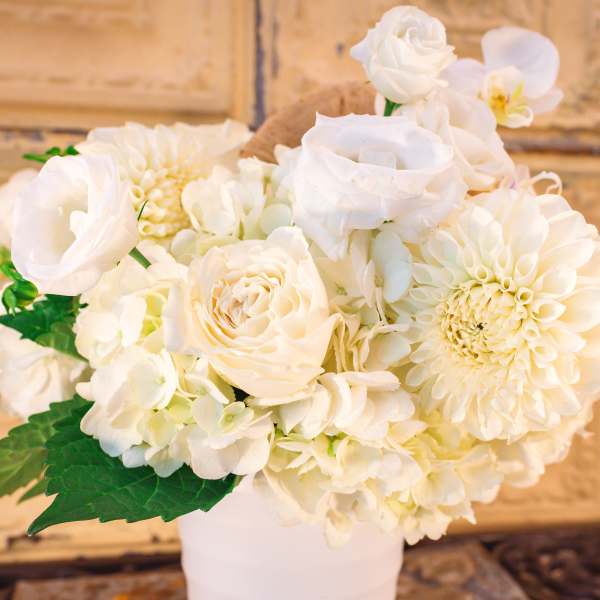 White floral arrangement in a white vase with roses and orchids