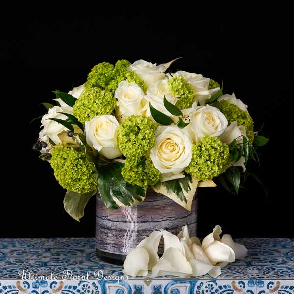 White roses and green hydrangea in a rustic vase with white calla lilies below