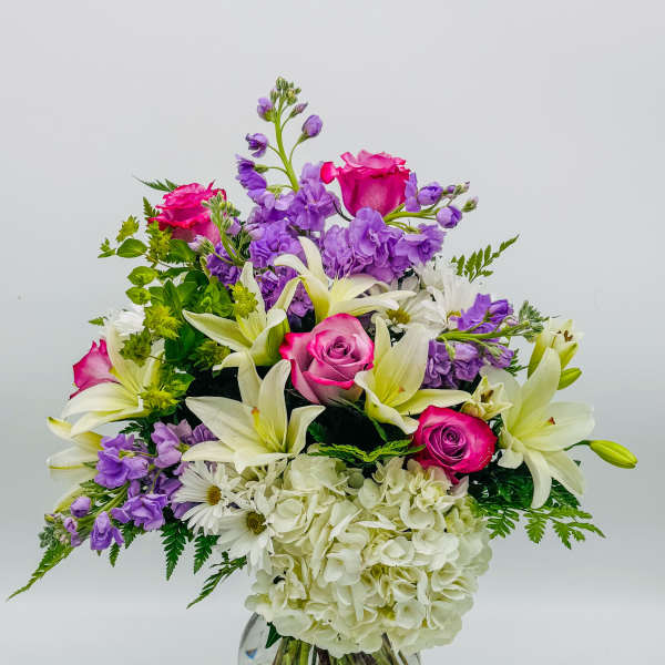 Mixed bouquet of pink roses, white lilies, purple flowers in a glass vase