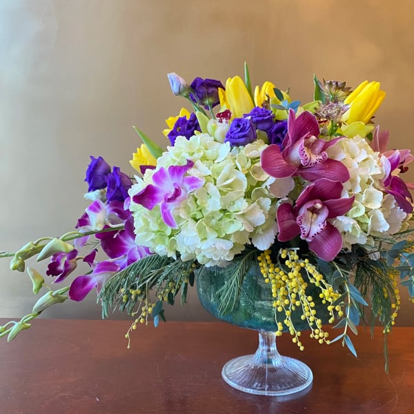 Mixed bouquet in a glass compote vase with purple, yellow, and white blooms