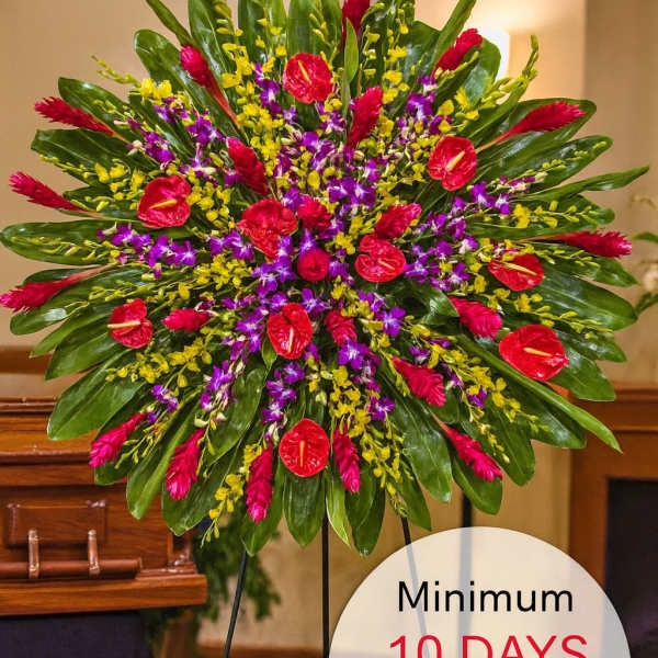 Large round tropical standing spray with red, purple, and yellow flowers on a metal easel in a funeral setting