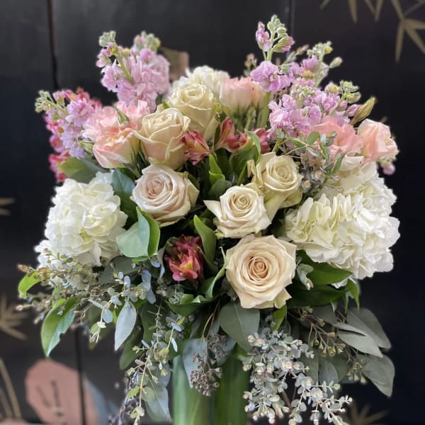 Bouquet of cream roses, pink blooms, and white hydrangeas in a glass vase
