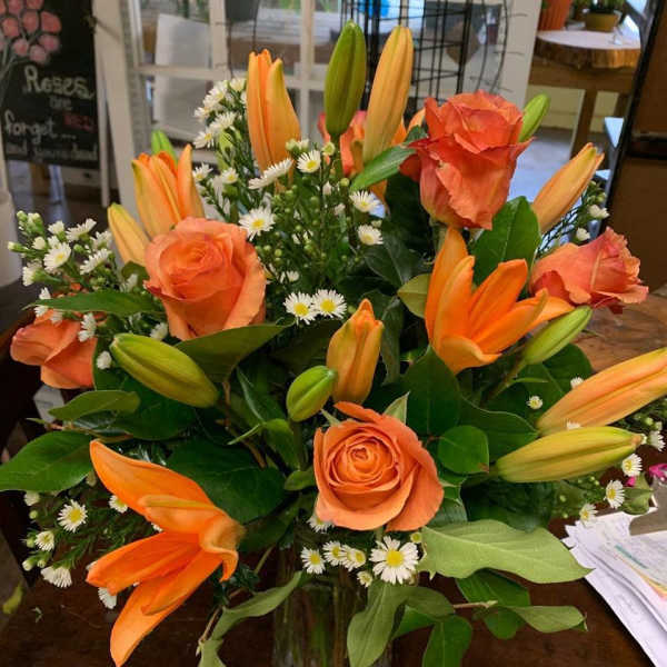 Orange roses and lilies with small white daisies in a glass vase