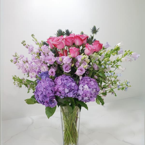 Pink roses and purple flowers arranged in a clear glass vase