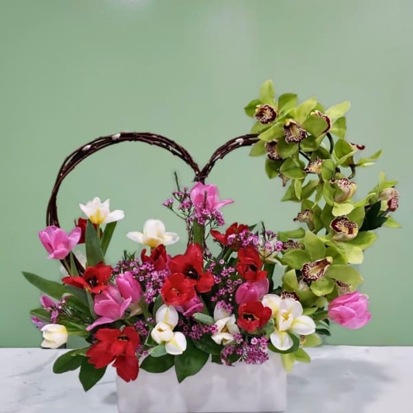 Heart-shaped floral arrangement with pink, red, white, and green blooms in a white box