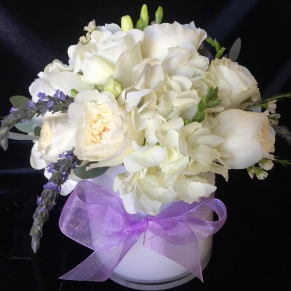 White floral bouquet in a white vase with a purple ribbon