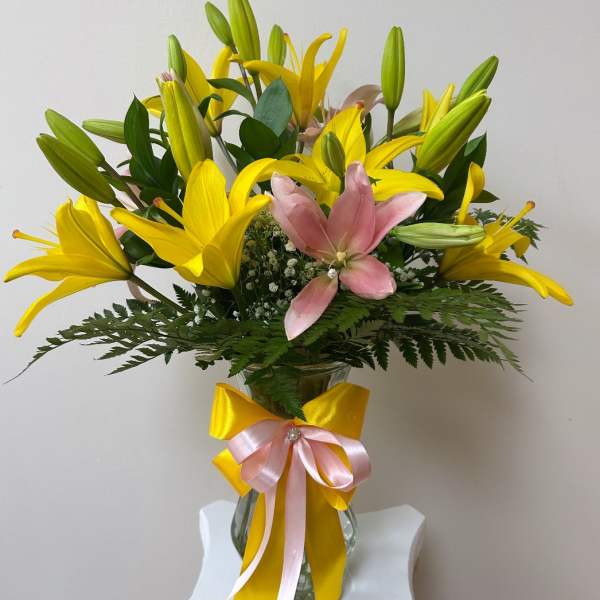 Yellow and pink lilies in a glass vase with a ribbon bow