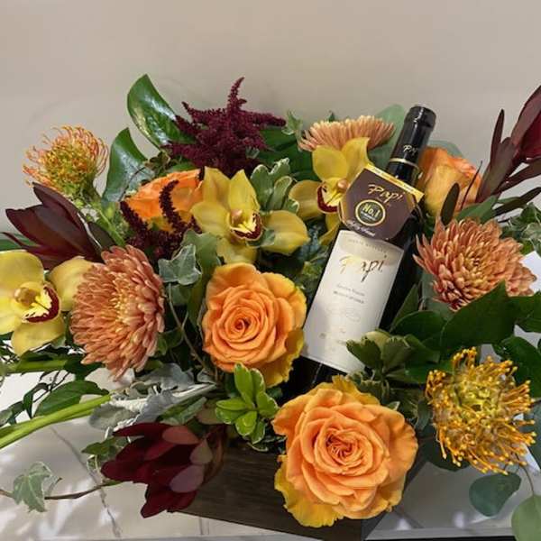 Mixed floral arrangement with a wine bottle in a square container