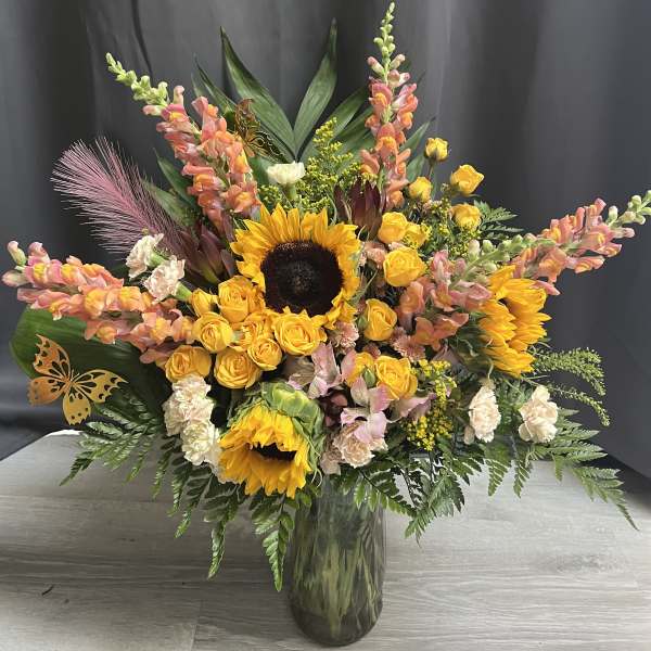 Large bouquet with sunflowers, yellow roses, and pink snapdragons in a glass vase