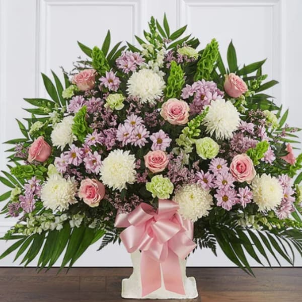 Large pink and white floral arrangement in a white vase with a pink ribbon